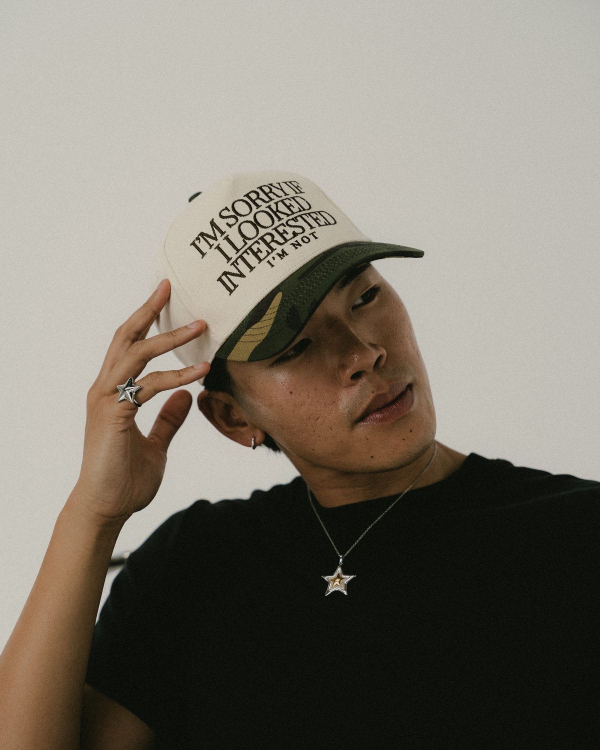 Model in a cream cap with a camo brim reading I'm sorry if I looked interested, I'm not.