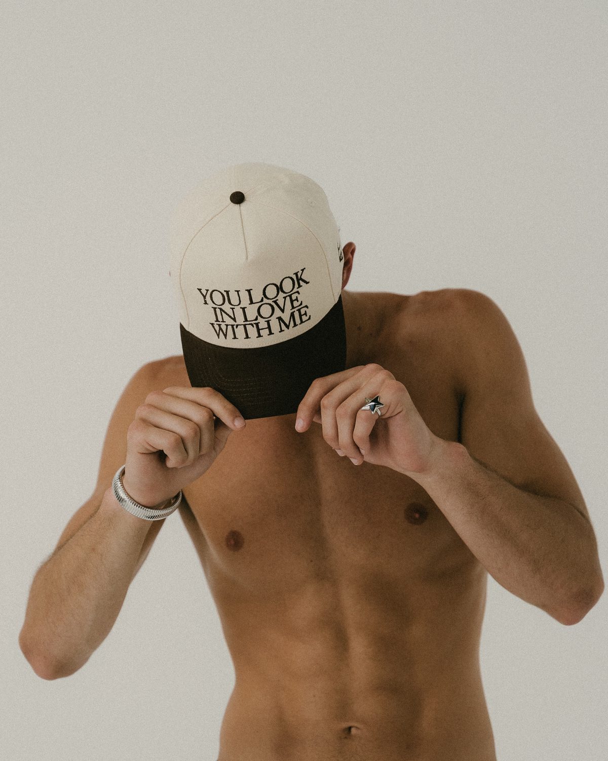 Model holding a cream and brown cap reading You look in love with me over his face.